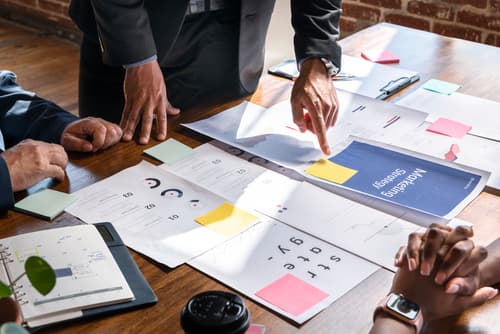 Team planning content calendar with documents and colorful sticky notes on wooden table